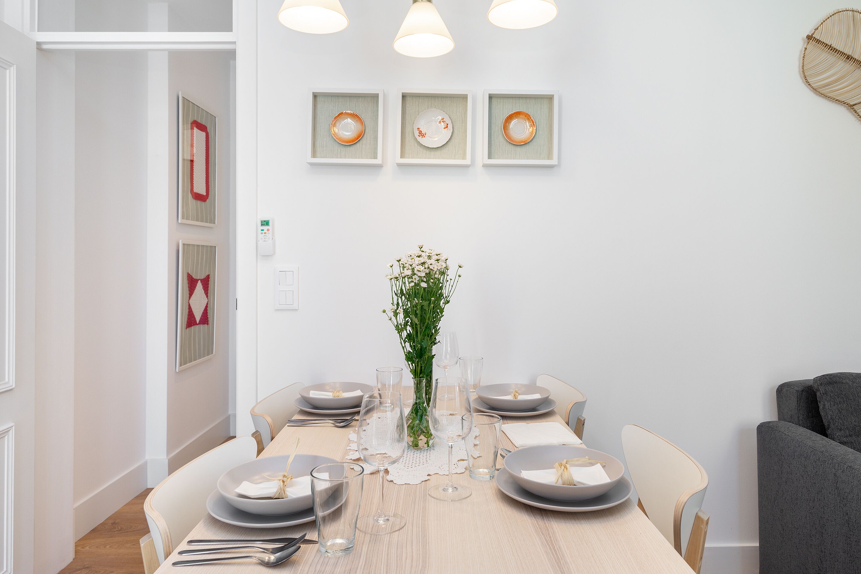 Een eetruimte met een tafel gedekt voor zes personen, inclusief borden, glazen en bestek. Daarboven hangen drie ingelijste gerechten aan de muur.