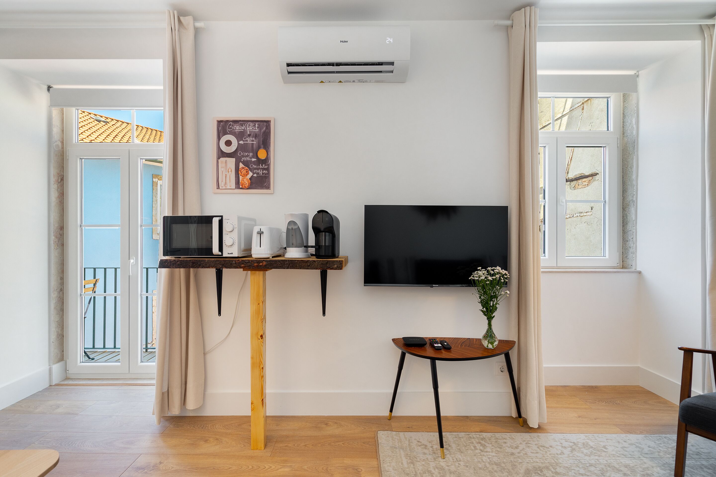 A modern living room with a flat-screen TV, a coffee machine, and a small table with a vase.