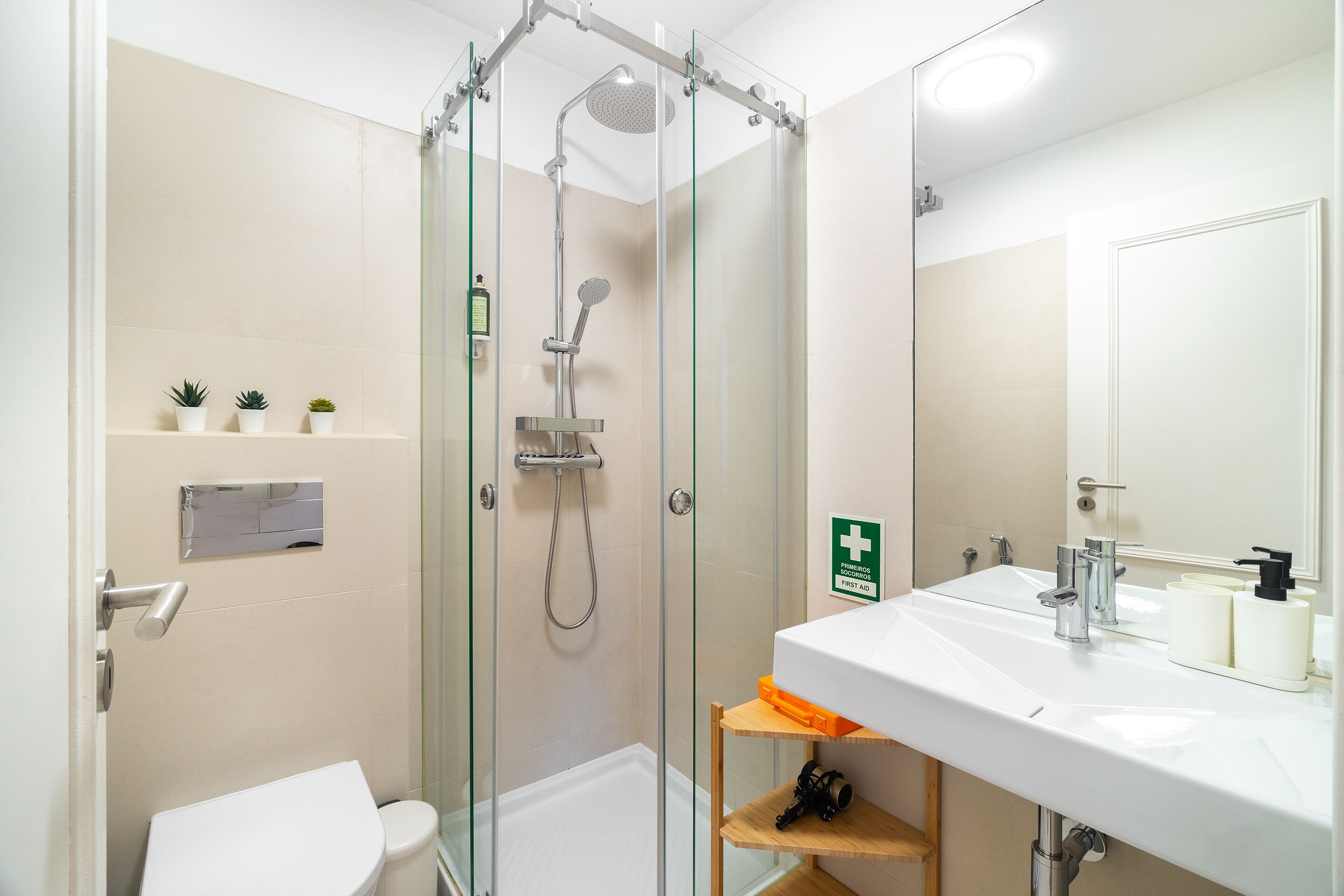 A modern bathroom with a glass-enclosed shower, a white sink, and a small shelf with toiletries.