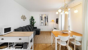 A modern living room with a sofa, dining table, and chairs. There is a microwave, a lamp, and a plant.