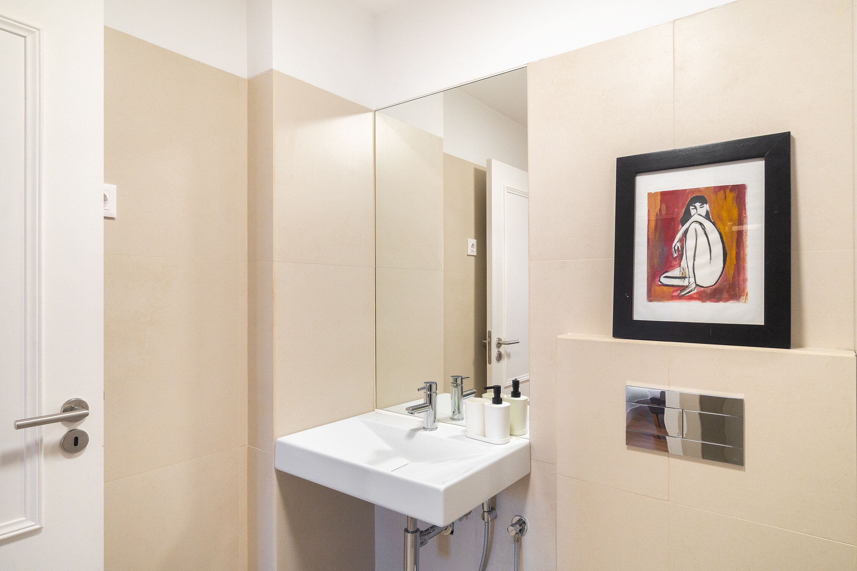 Un baño moderno con un lavamanos blanco, un espejo grande y una obra de arte enmarcada en la pared.