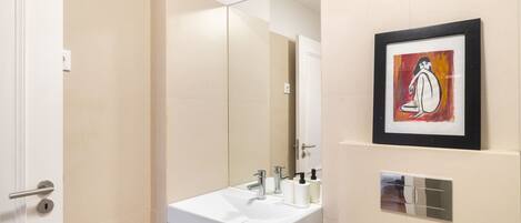Un baño moderno con un lavamanos blanco, un espejo grande y una obra de arte enmarcada en la pared.