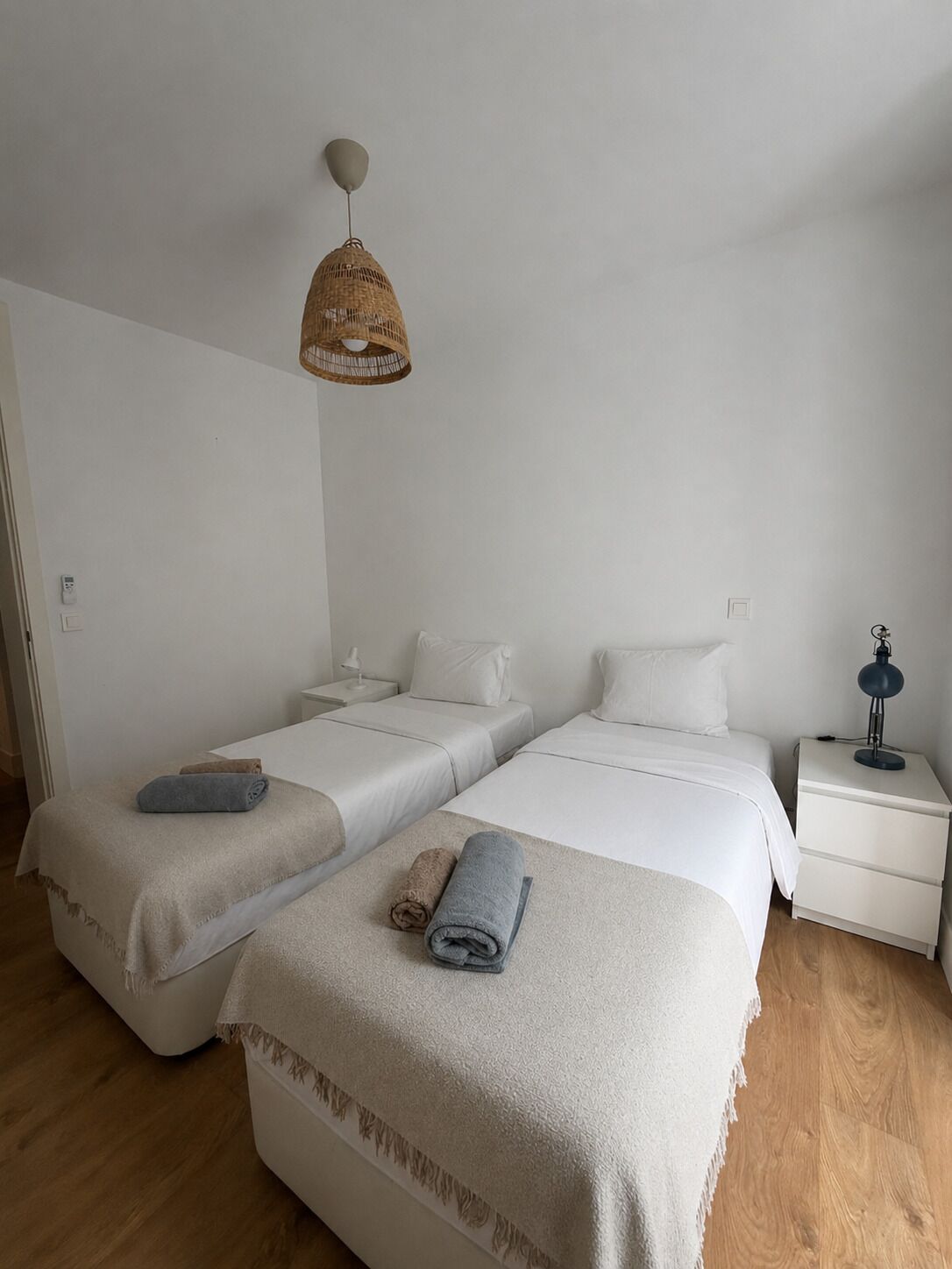 Un dormitorio minimalista con dos camas, una mesita de noche con lámpara y una lámpara colgante.