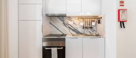 A compact kitchen with white cabinetry, a marble backsplash, and stainless steel appliances.