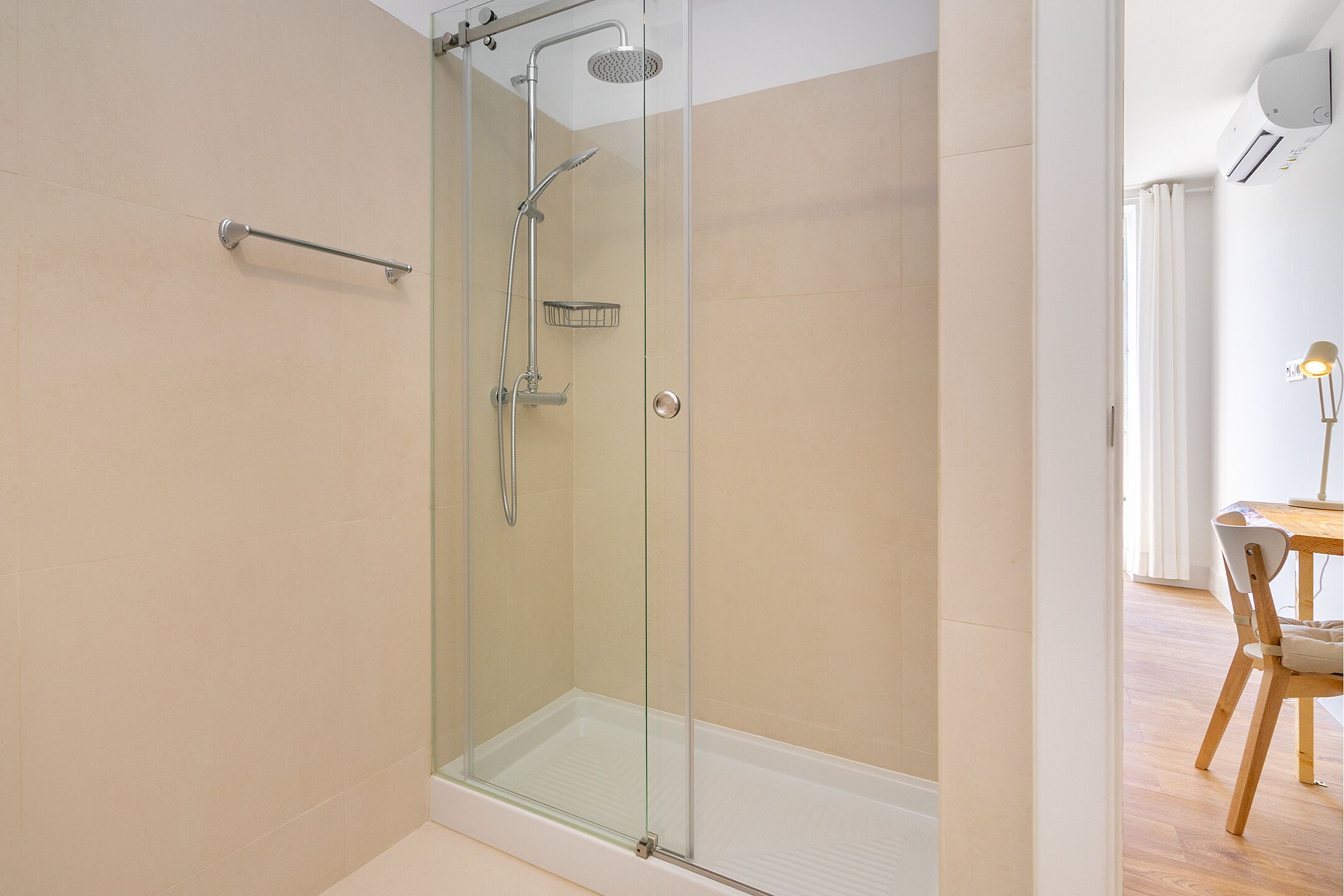 Un bagno moderno con doccia vetrata, portasciuga e una sedia di legno in zona pranzo.