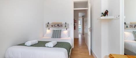 A modern hotel room with a large bed, a wooden bench, and a hallway leading to another room.
