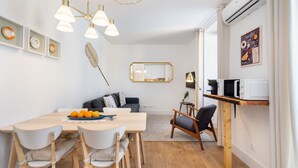 A modern kitchen with a wooden table, white chairs, a dining area, and a built-in microwave shelf.
