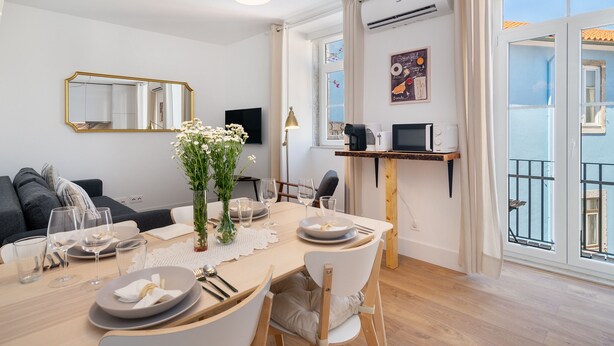 A modern dining area with a wooden table set for four, a large mirror, and a view of the balcony.