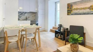 A modern kitchen with white cabinets, a dining area with a table and chairs, and a painting on the wall.