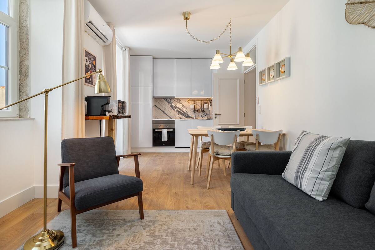 A modern living room with a sofa, armchair, and a dining area with a table and chairs.