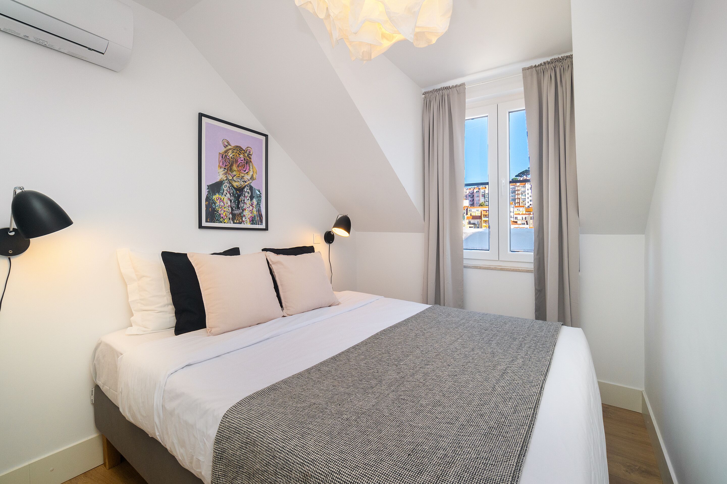 A neatly made bed with a patterned blanket, a framed artwork on the wall, and a window with curtains.