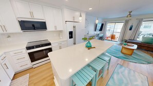 A modern kitchen with white cabinetry, a central island with stools, a built-in oven, and a microwave. - SPC3209 is an upstairs 2 BR with Canal Views by RedAwning (Destin)