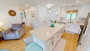 A modern kitchen with white cabinets, a central island, and a dining area with a grey sofa. - SPC3209 is an upstairs 2 BR with Canal Views by RedAwning (Destin)