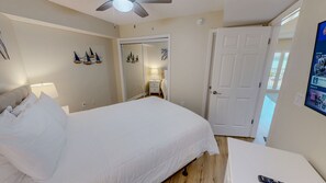 A bedroom with a bed, a nightstand, a lamp, a ceiling fan, and a door.