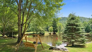 A serene outdoor setting with a wooden swing, a pond, and a small waterfall. - Twin Ponds Retreat-Pond/Hot Tub/Fire Pit/Game Room/Pet Friendly by RedAwning (Whittier)
