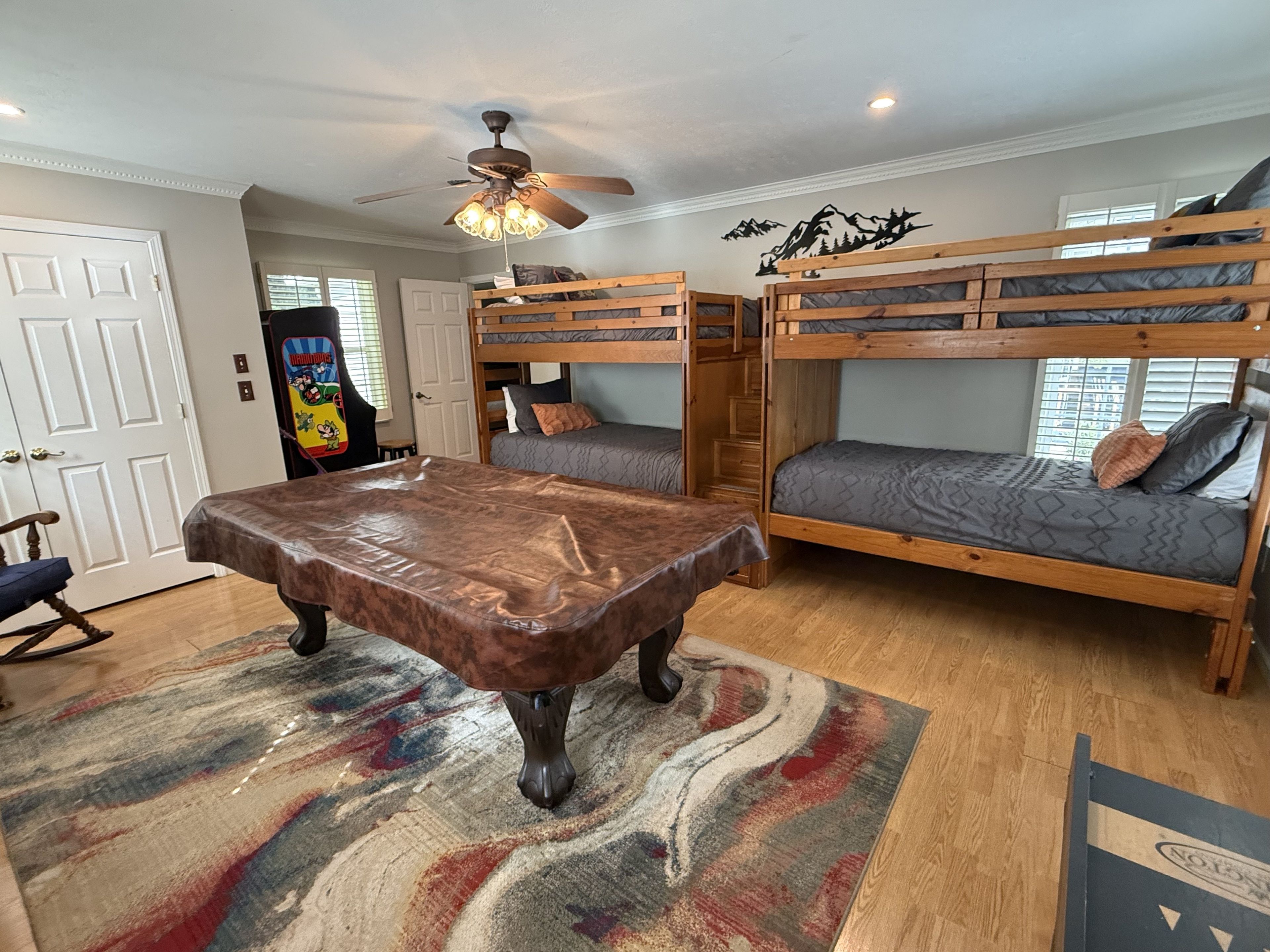 A room with bunk beds, a ceiling fan, a table, and a colorful rug.