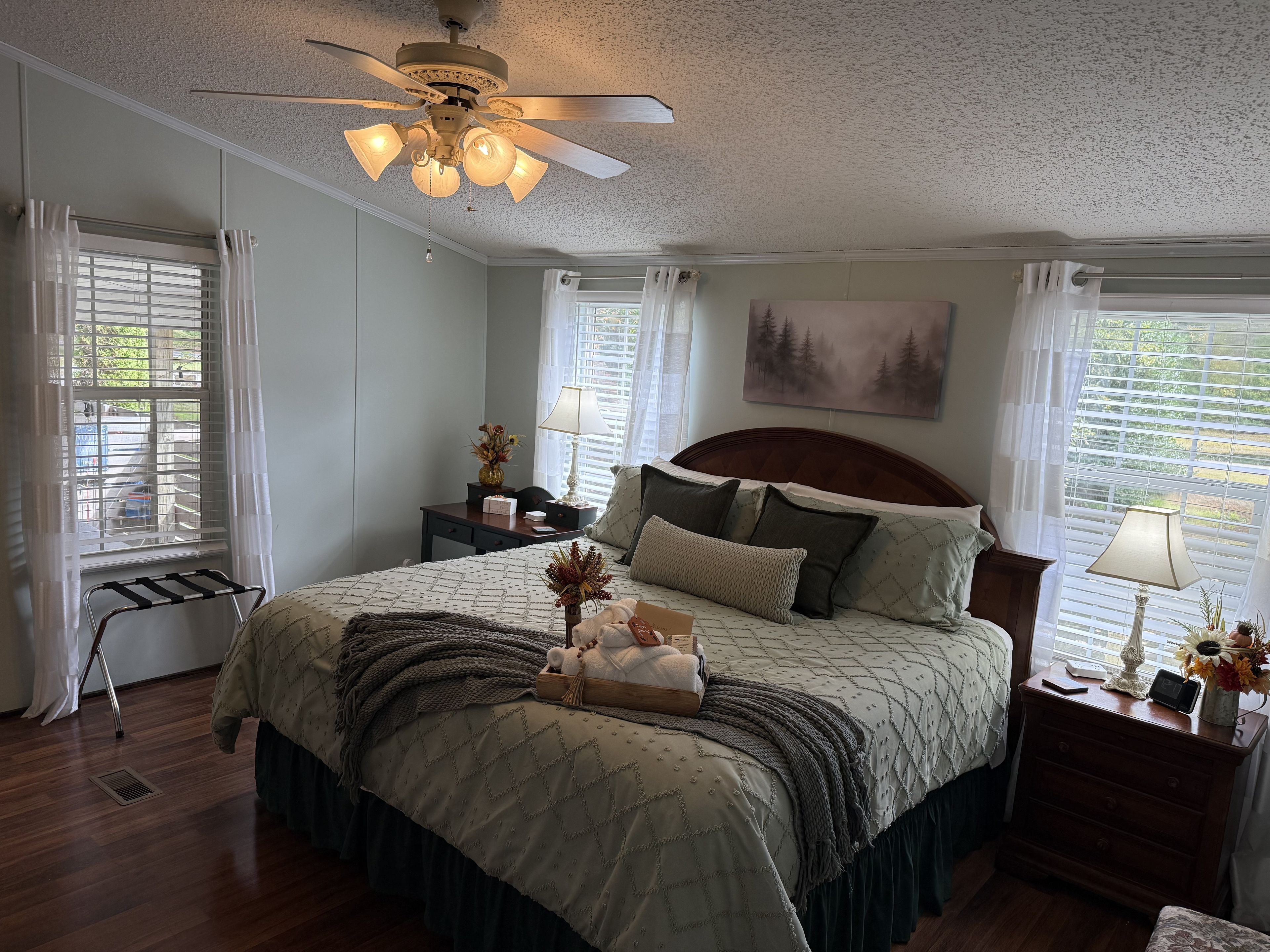 Une chambre à coucher avec un lit, des tables de chevet, un ventilateur de plafond et une fenêtre avec des stores.