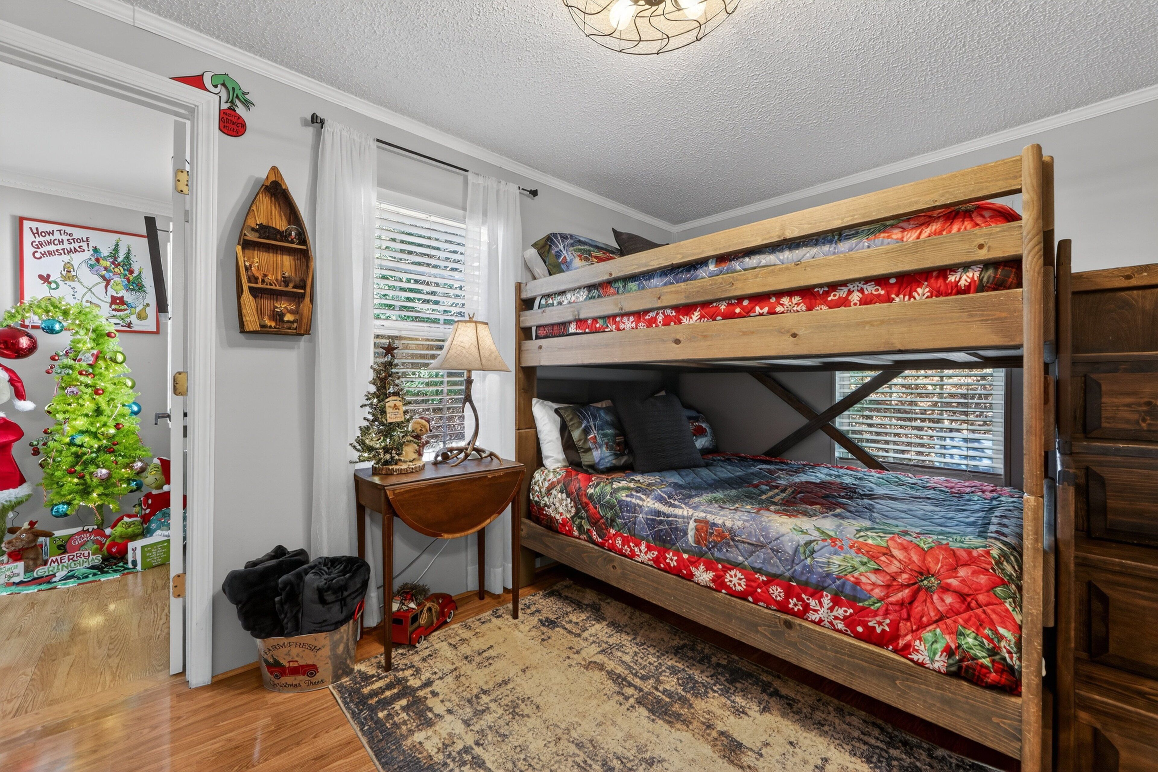 Una cama litera con colcha estampada, una mesita de madera, un árbol de Navidad y un estante fijado a la pared.