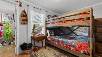 Una cama litera con colcha estampada, una mesita de madera, un árbol de Navidad y un estante fijado a la pared.