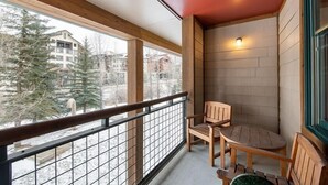 Een balkon met een houten leuning, twee houten stoelen en een kleine tafel.
