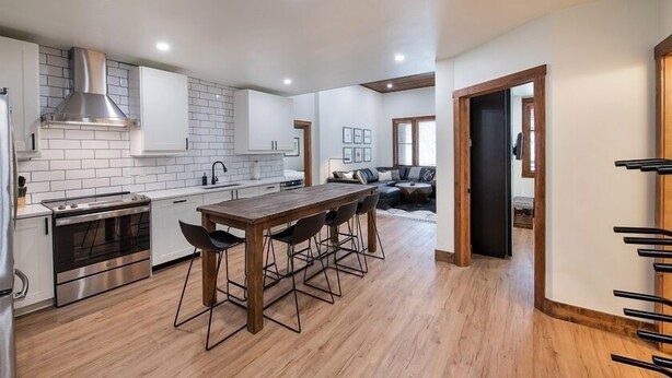 Een moderne keuken met een centraal eiland, roestvrijstalen apparatuur, en een eethoek met een houten tafel en stoelen.