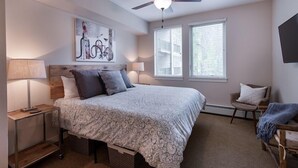 Une chambre à coucher avec un lit, des lampes de chevet, un ventilateur de plafond, une fenêtre et une chaise.