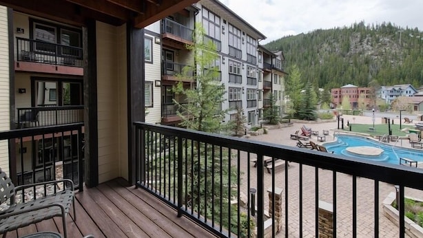 Un balcon offrant une vue sur un espace piscine, une terrasse en bois et un paysage montagneux en arrière-plan.