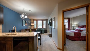 A modern kitchen with a granite countertop and a dishwasher, a dining area with a table and chairs, a living room with a sofa and a TV, and a bedroom with a bed and a window. - Mountain View Ski-In Ski-Out Condo - Zephyr Mountain Lodge Premium-Rated 2516 (Winter Park)