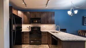 A modern kitchen with dark wooden cabinets, a black refrigerator, a microwave, an oven, and a sink. - Mountain View Ski-In Ski-Out Condo - Zephyr Mountain Lodge Premium-Rated 2516 (Winter Park)