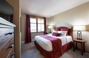 A hotel room with a bed, bedside lamps, a TV, and a window with curtains. - Mountain View Ski-In Ski-Out Condo - Zephyr Mountain Lodge Premium-Rated 2516 (Winter Park)