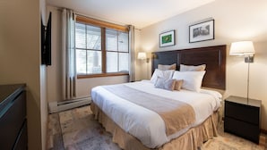 Une chambre d’hôtel avec un grand lit, deux lampes de chevet, un téléviseur à écran plat et une fenêtre avec des stores.