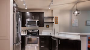 Une cuisine moderne dotée d’appareils électroménagers en acier inoxydable, de meubles de rangement aux couleurs sombres et d’un plan de travail blanc.