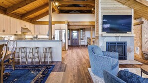 A spacious living area with a large TV, wooden beams, a fireplace, and a bar area with stools. - AMAZING VIEWS- MODERN HOME- SH #14 by Bear Valley Vacation Rentals (Arnold)