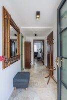 Un pasillo con un espejo grande y decorativo, un banco, un perchero y una puerta que da a otra habitación.