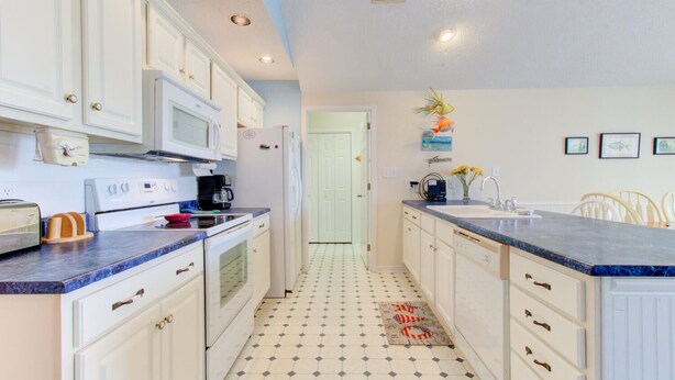 A narrow kitchen with white cabinets, a microwave, a stove, and a sink.