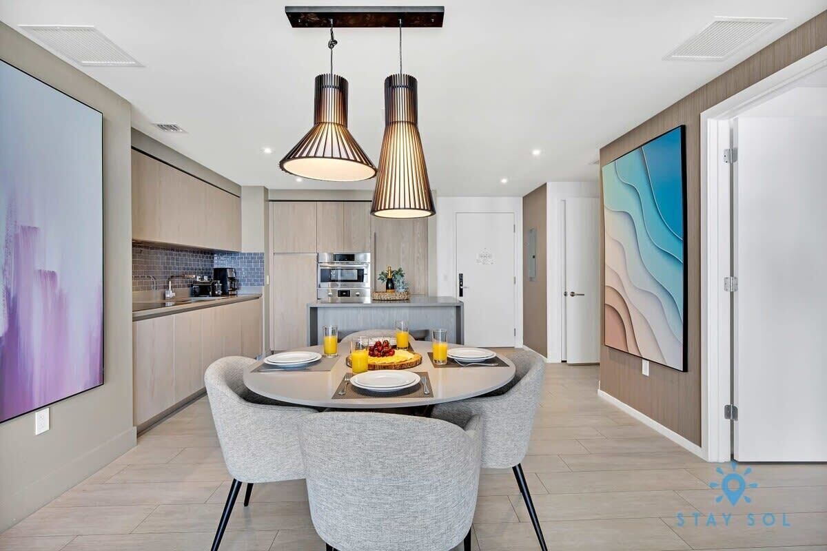 Une cuisine moderne avec un coin repas, comprenant une table ronde entourée de chaises, des luminaires suspendus et un grand tableau accroché au mur.