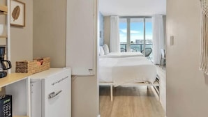 Une chambre d’hôtel équipée d’un lit, d’un minibar, d’un petit bureau avec une machine à café et offrant une vue sur la ville grâce à de grandes fenêtres.