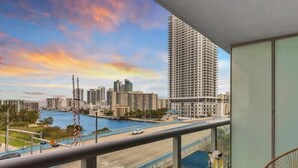 Un balcon offrant une vue sur le paysage urbain, avec des immeubles de grande hauteur et une étendue d’eau.