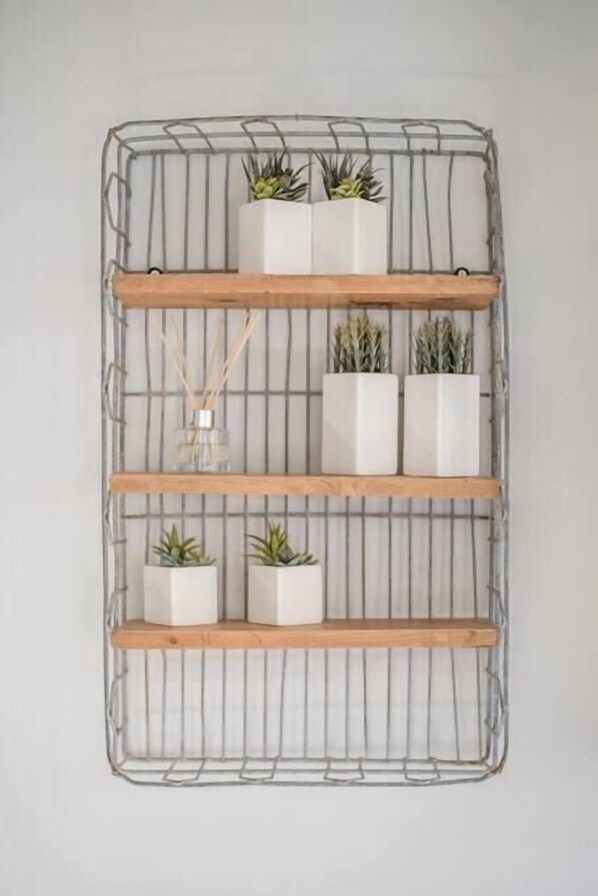 Une étagère métallique fixée au mur, composée d’une structure en treillis et de trois étagères en bois, chacune supportant des pots blancs contenant des plantes vertes.