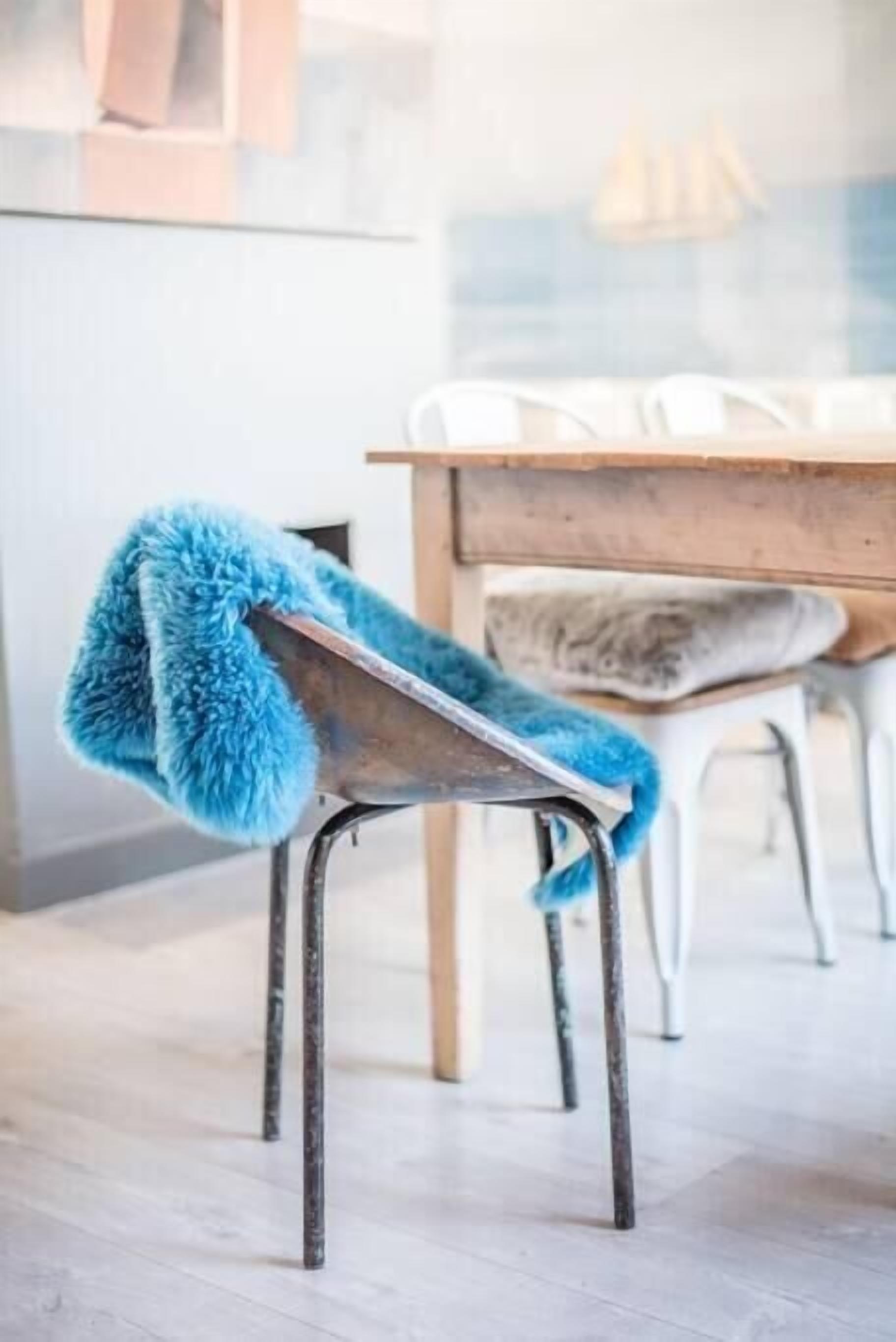 Una silla con un plaid azul y mullido, una mesa de madera y sillas blancas en un interior moderno.