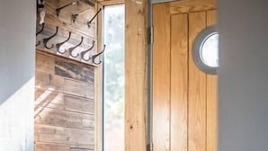 A corner of a room with a wooden door, a window with a view, and a coat rack with several coats.