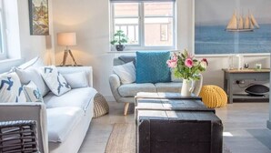 A modern living room with a sofa, a coffee table, and a window with a view of the sea.