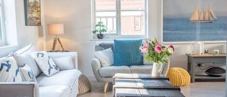 A modern living room with a sofa, a coffee table, and a window with a view of the sea.