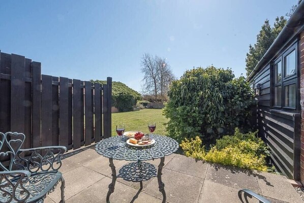 Pihalla on terassi, jossa on pyöreä pöytä katettuna kahdelle hengelle, ja pöydällä on ruokaa ja juomia.