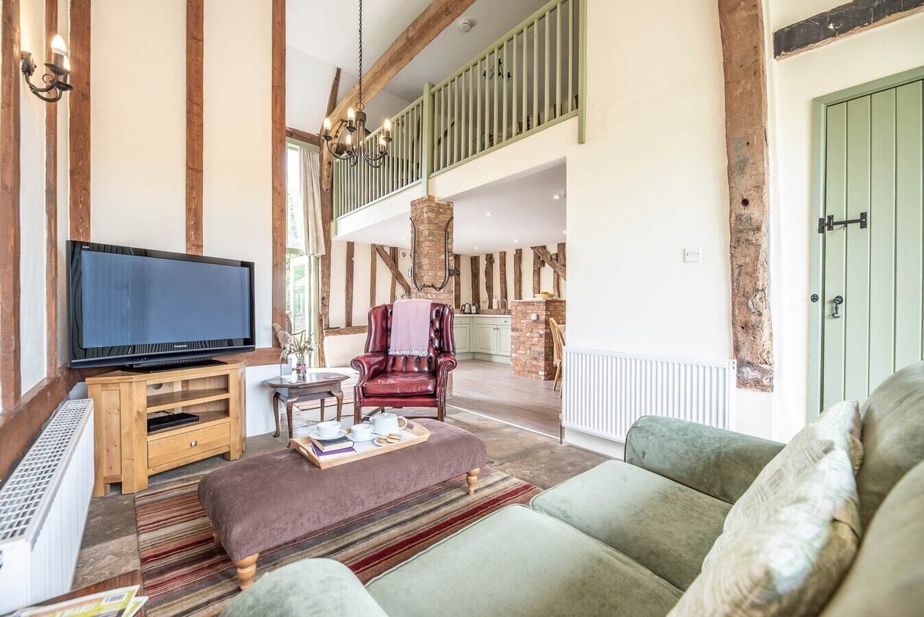 A spacious living area with a large flat-screen TV, a leather armchair, a sofa, and a wooden entertainment unit.