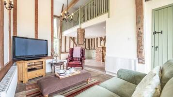 A spacious living area with a large flat-screen TV, a leather armchair, a sofa, and a wooden entertainment unit.