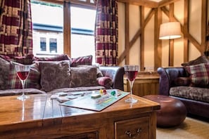 Un salon chaleureux avec une table basse en bois, deux verres de vin rouge, un jeu de société et une lampe.