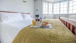 A neatly made bed with white linens, a tray with croissants, a cup of coffee, and a glass of orange juice. - The Links, Southwold (Southwold)