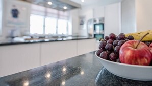 A modern kitchen with a marble countertop, a bowl of fruit, and a window with natural light. - The Links, Southwold (Southwold)