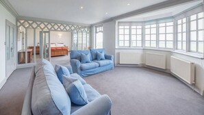 A spacious living room with a large window, a blue sofa, and a wooden coffee table. - The Links, Southwold (Southwold)